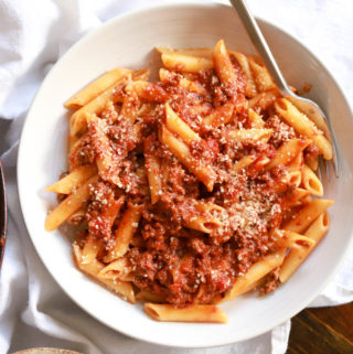 white bowl with penne and meat sauce over a white napkin.