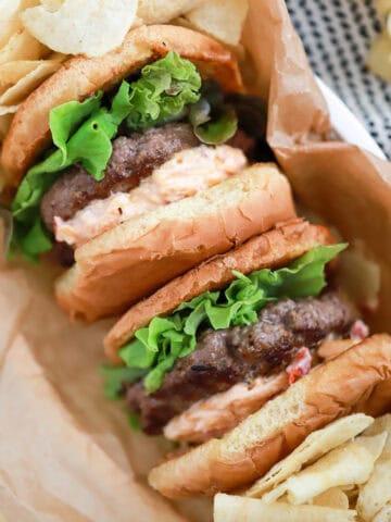A hamburger with lettuce, tomato, and pimento cheese on parchment paper.