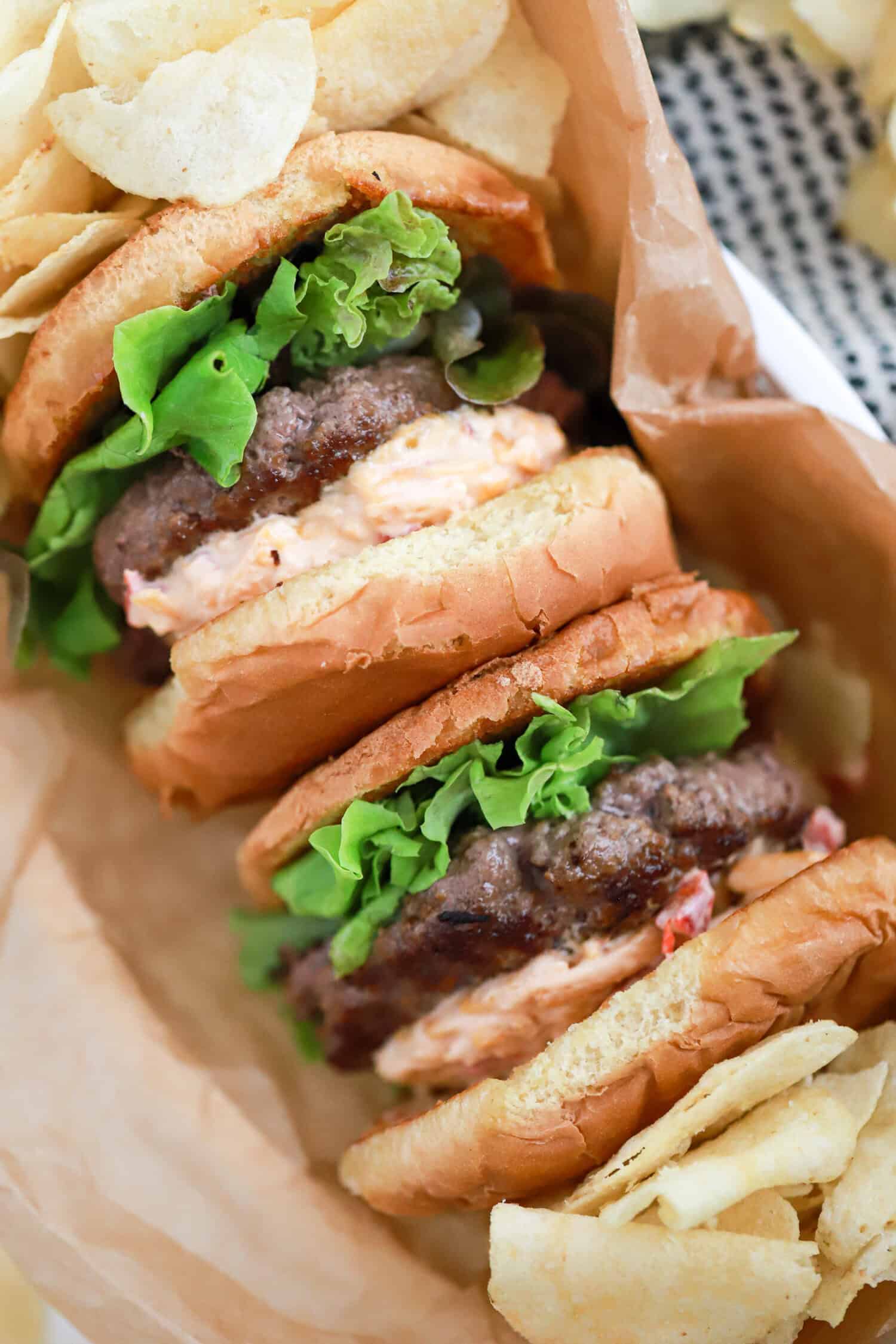 A hamburger with lettuce, tomato, and pimento cheese on parchment paper.