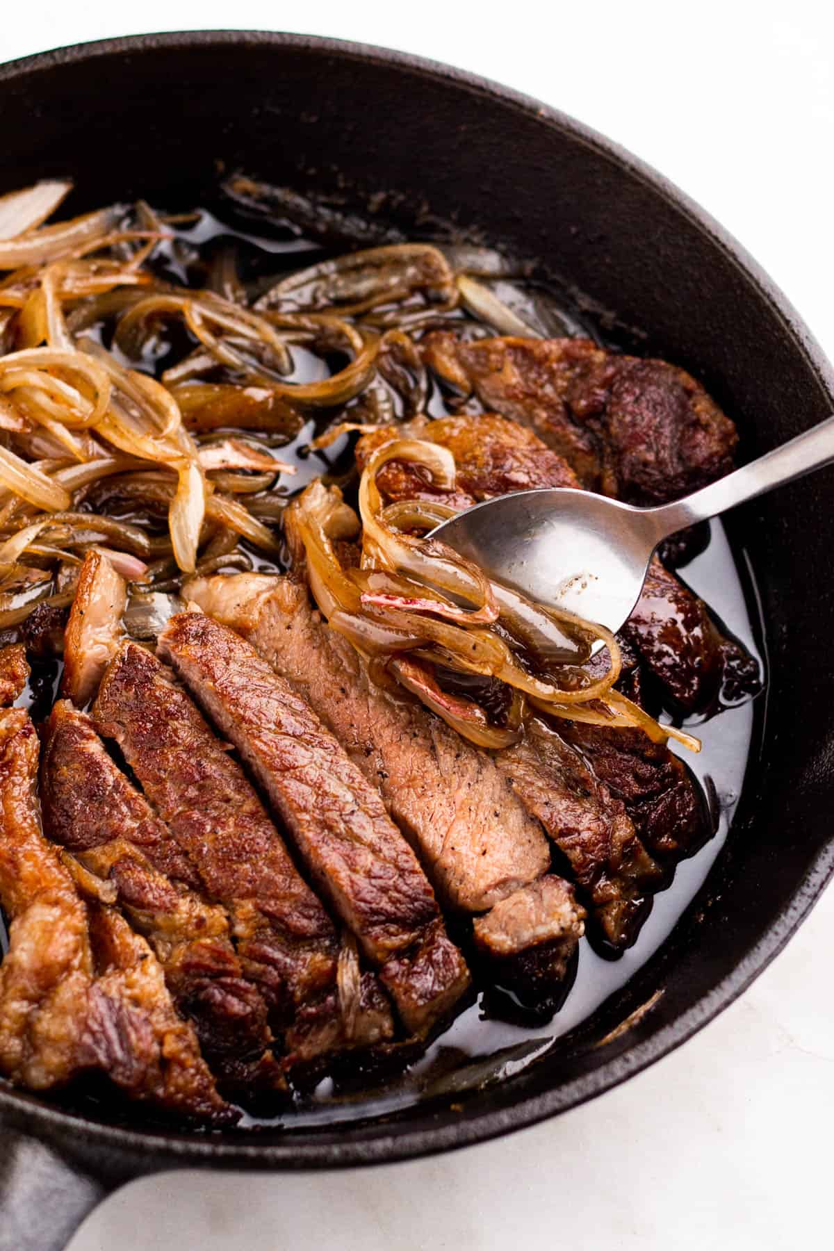 Black skillet with sliced steak and shallot sauce.