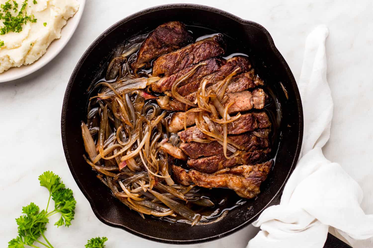 Cast iron skillet of ny strip steak and seared shallots.