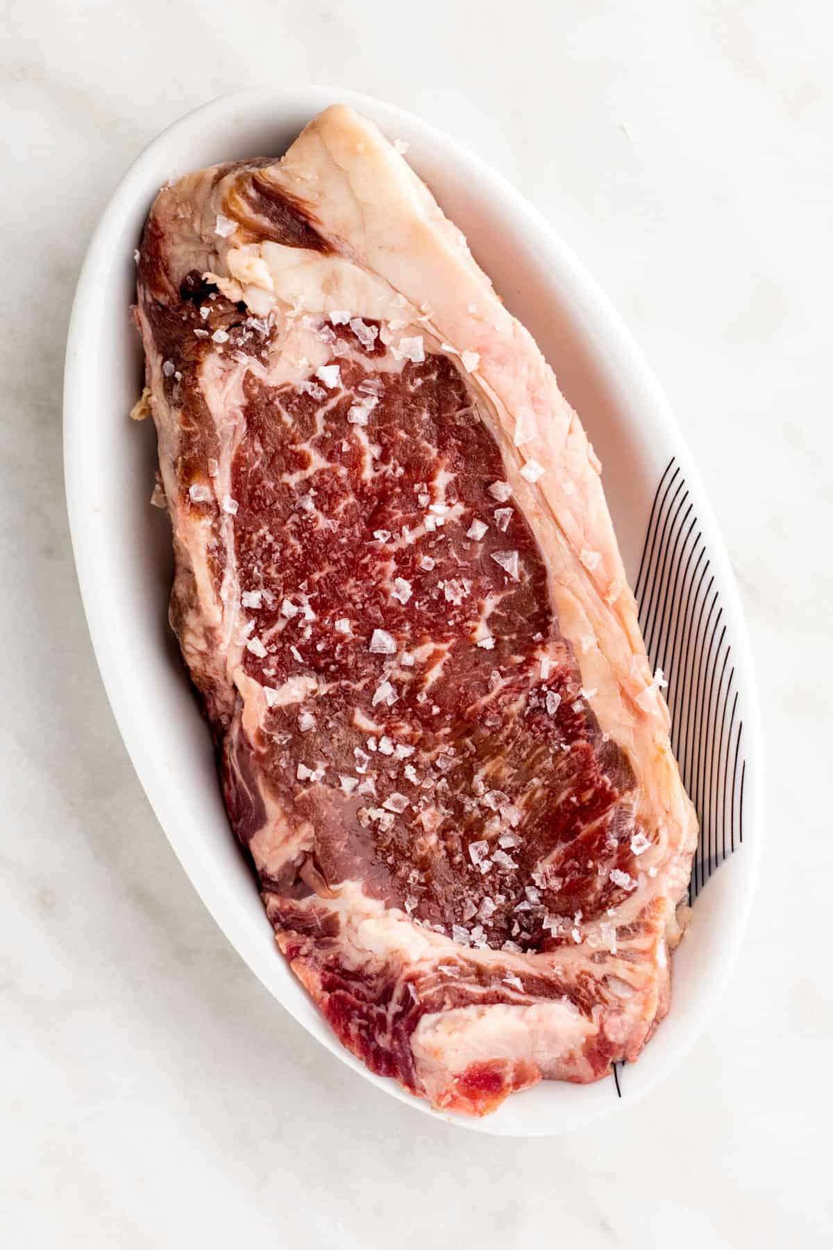 Strip steak salted in a small white dish.