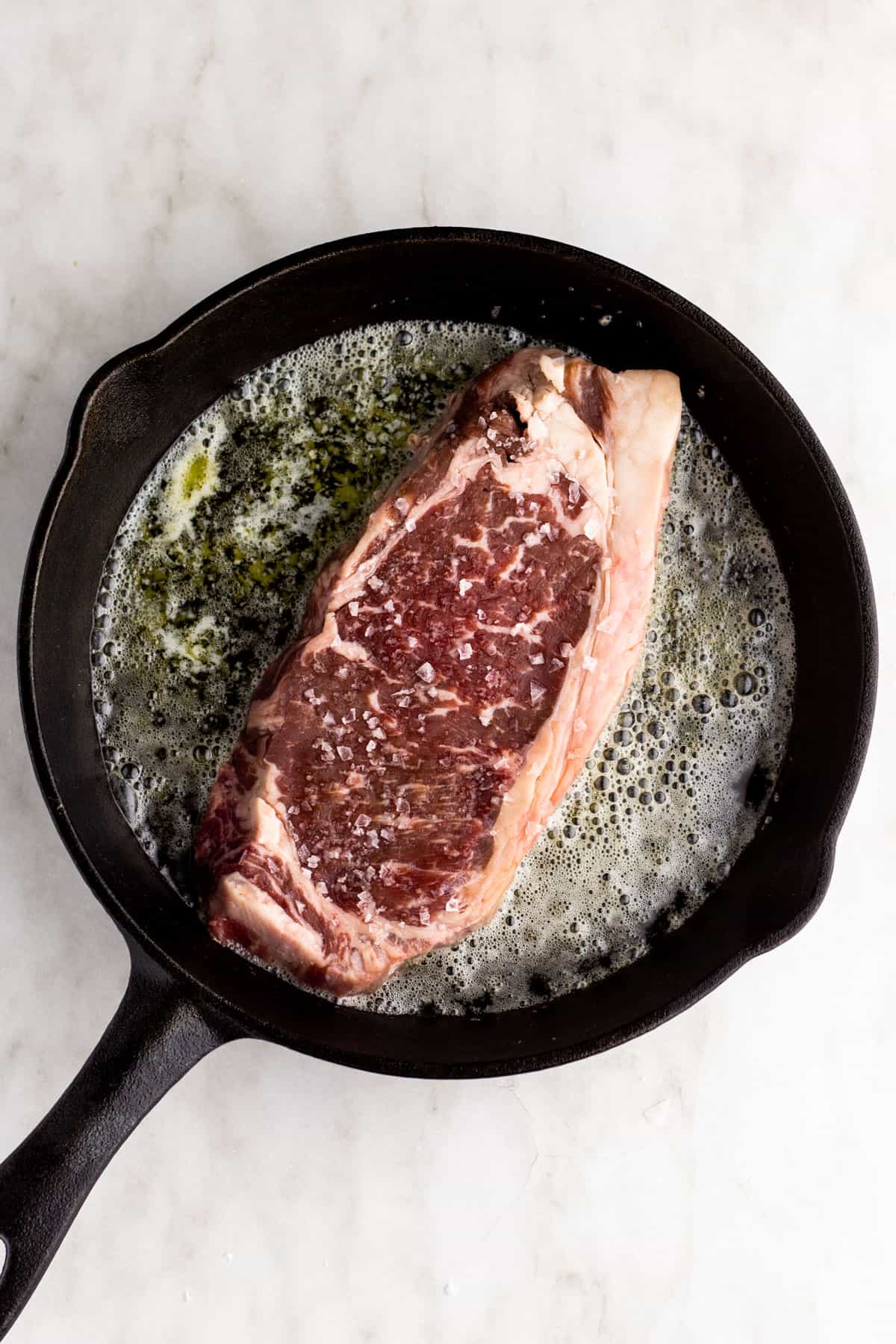 Steak cooking on first side in cast iron skillet.