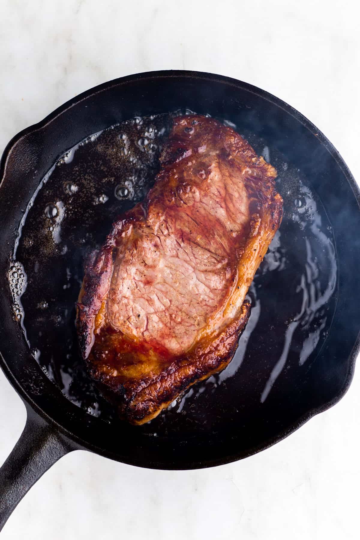Seared steak in a skillet with butter and steam rising up.