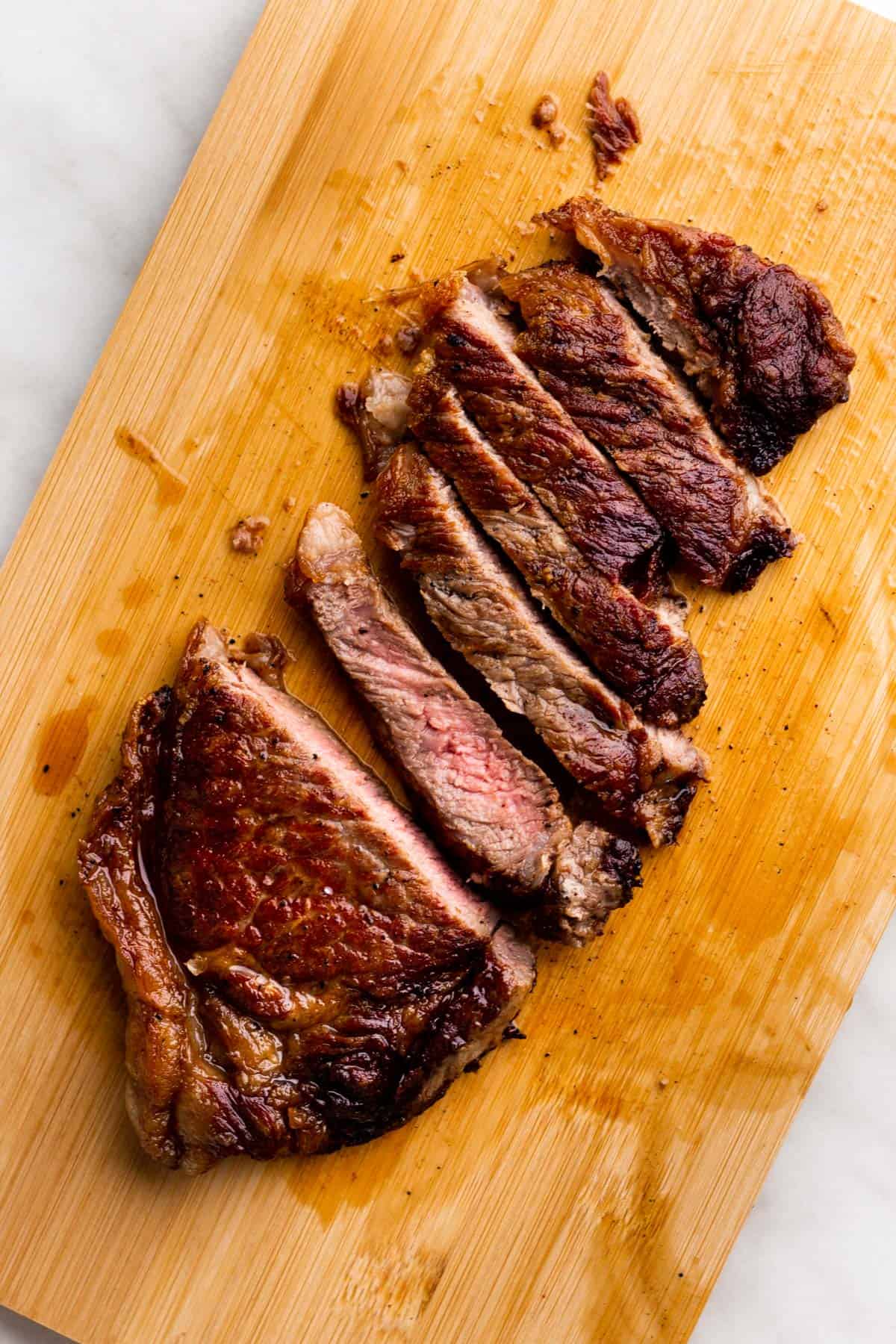 Sliced NY Strip on light wooden board.