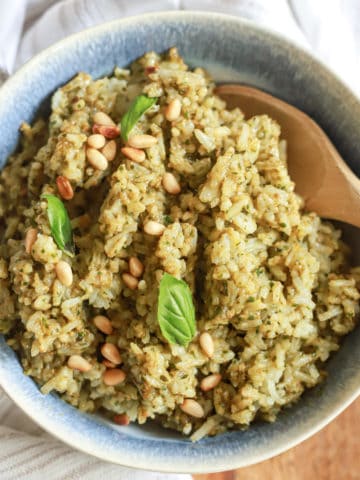 blue bowl of pesto rice with wooden spoon and basil leaves