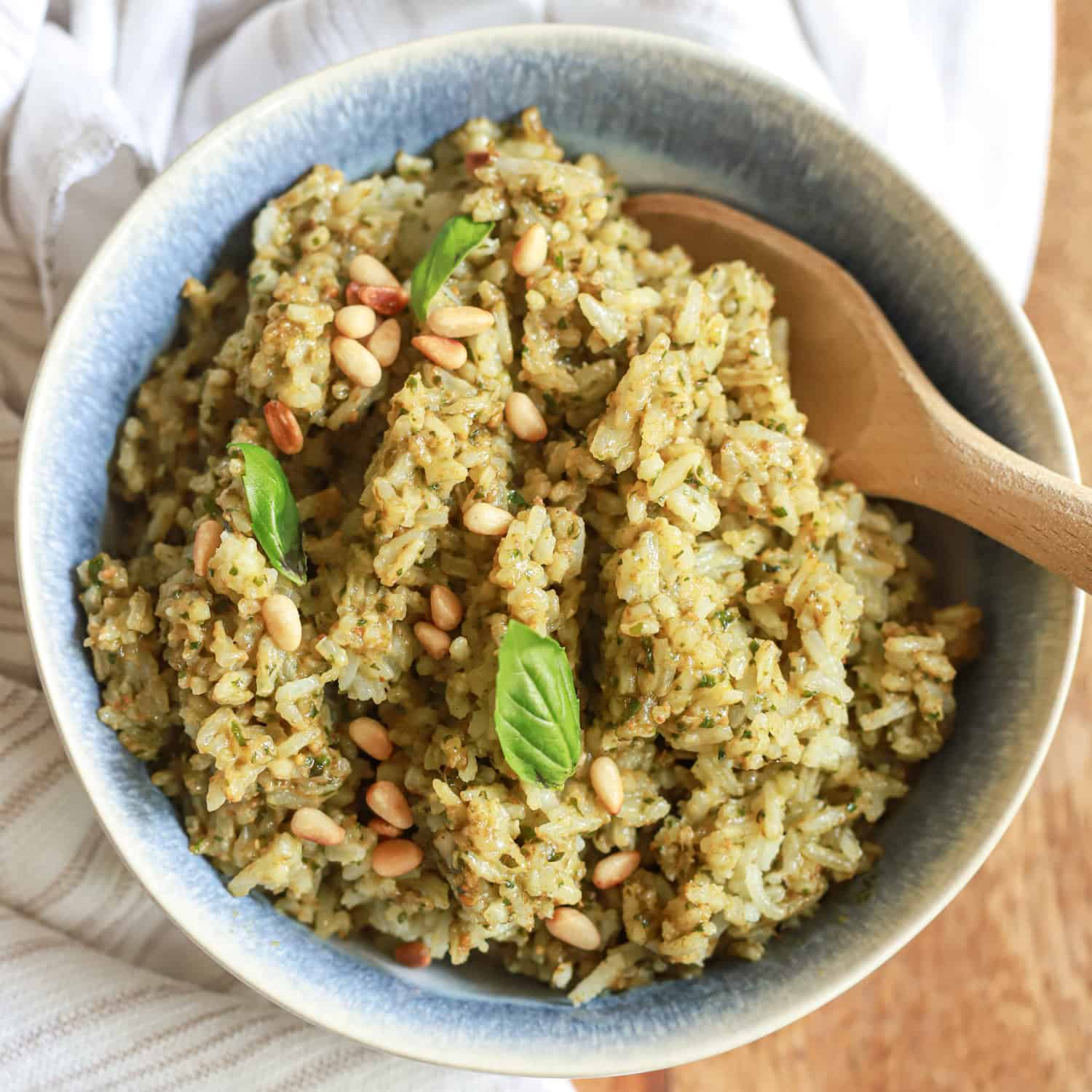 blue bowl of pesto rice with wooden spoon and basil leaves