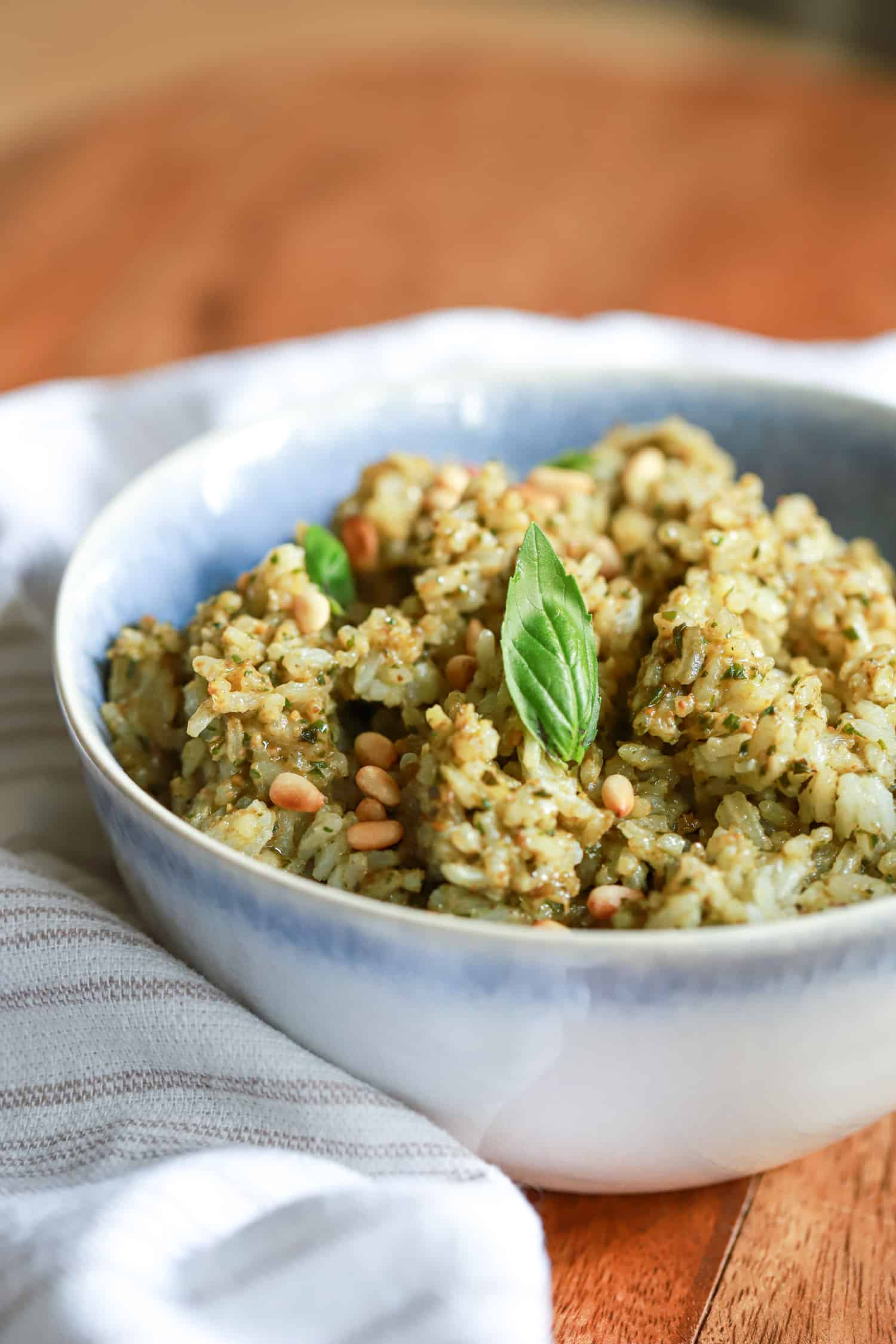 side view pesto rice with basil leave and pine nuts in blue bowl