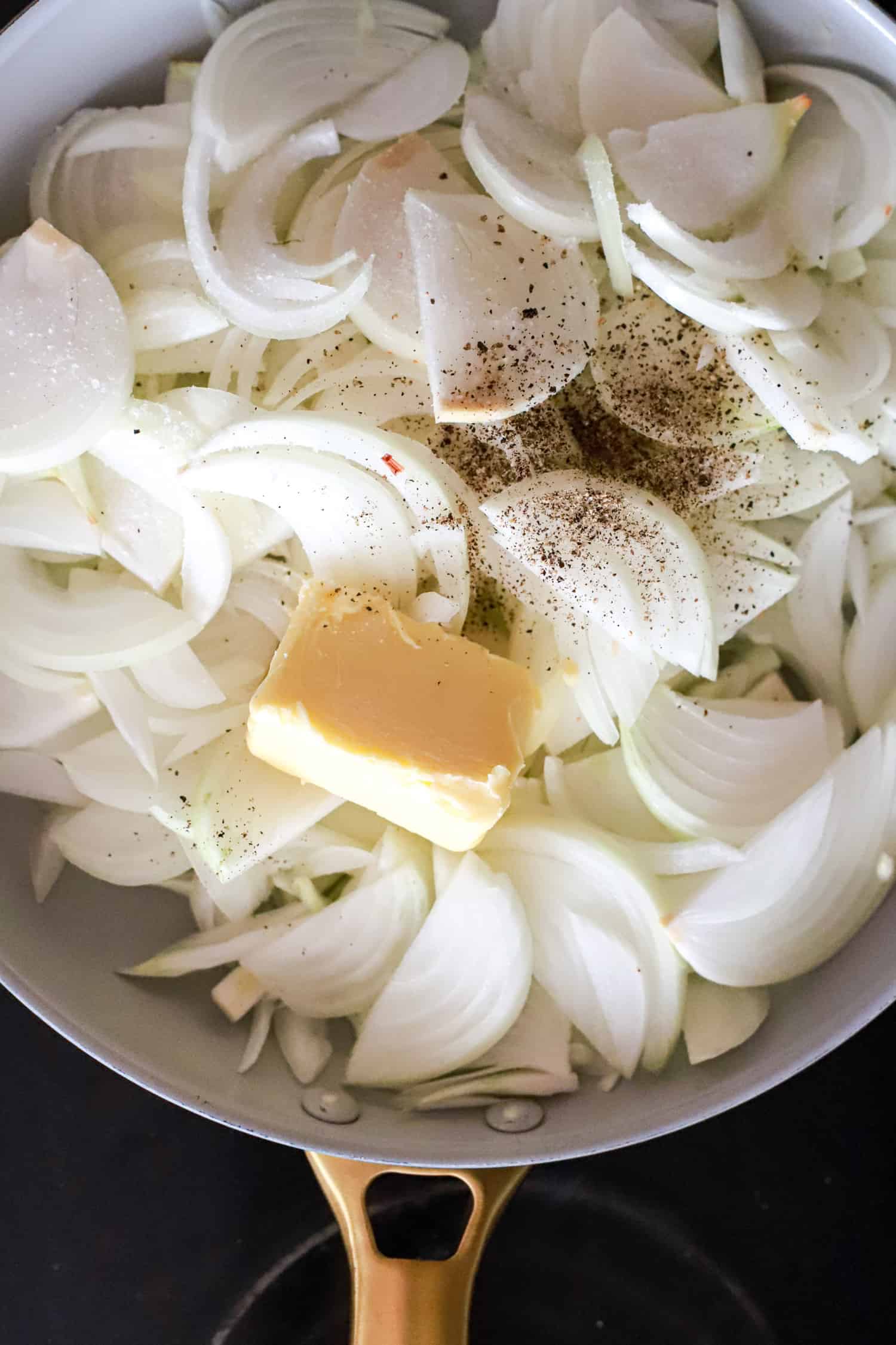 raw sliced onions in a skillet with butter and pepper.