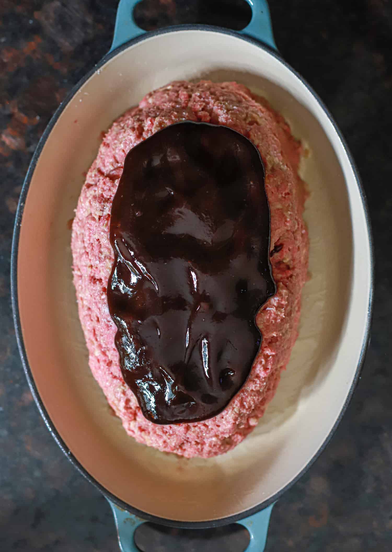 raw meatloaf in oval baking dish topped with balsamic glaze.