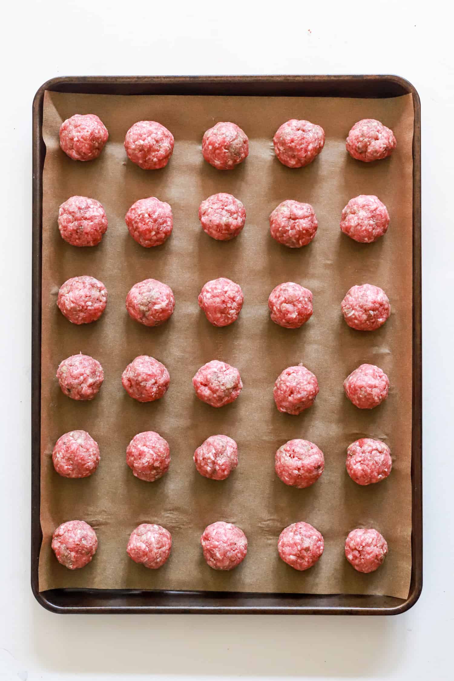 baking sheet of ground beef meatballs before being baked.