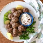 white plate with lemon wedges, herbs, and greek meatballs.