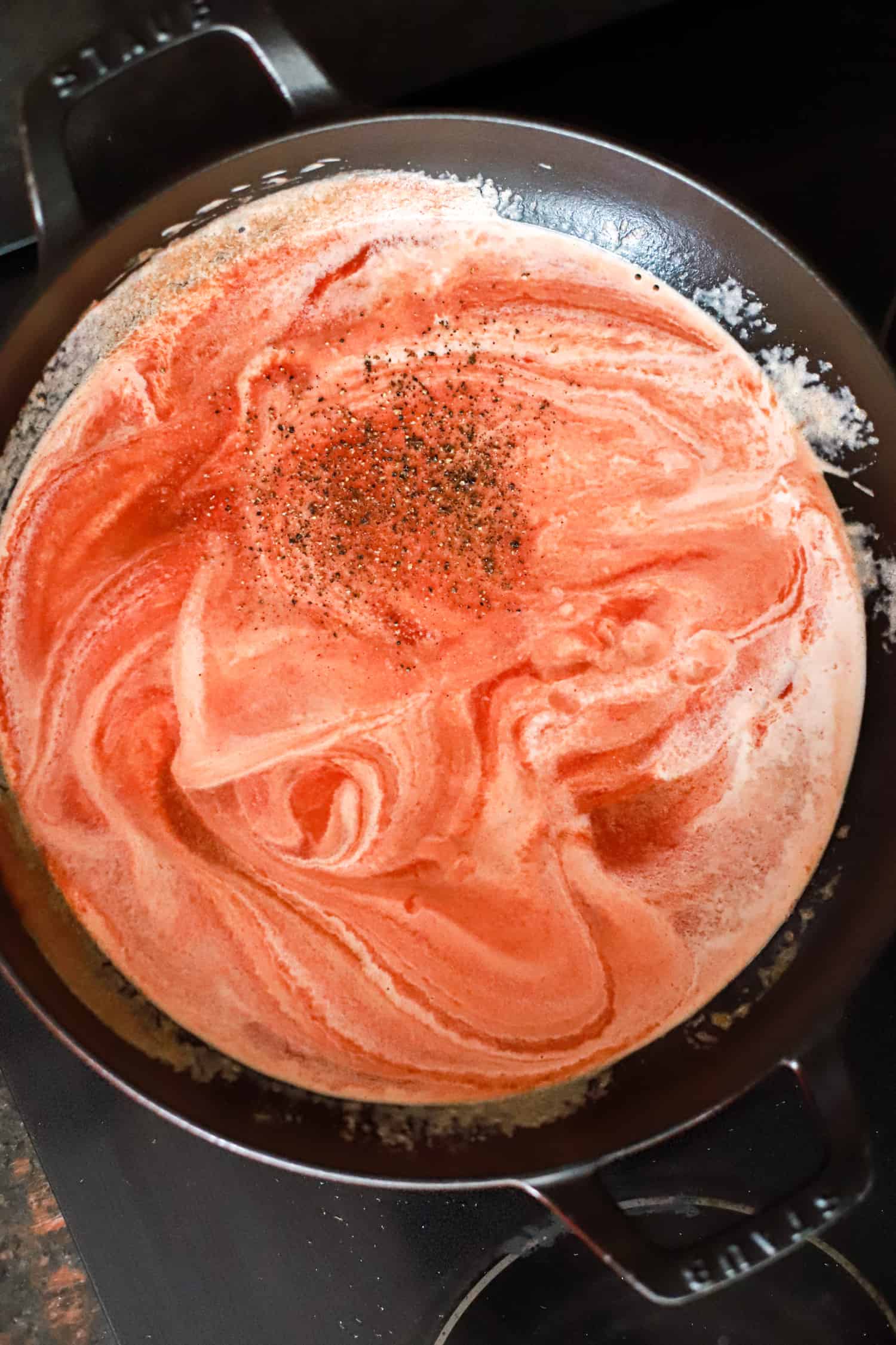 marbled look pink pasta sauce in black skillet with pepper flakes.
