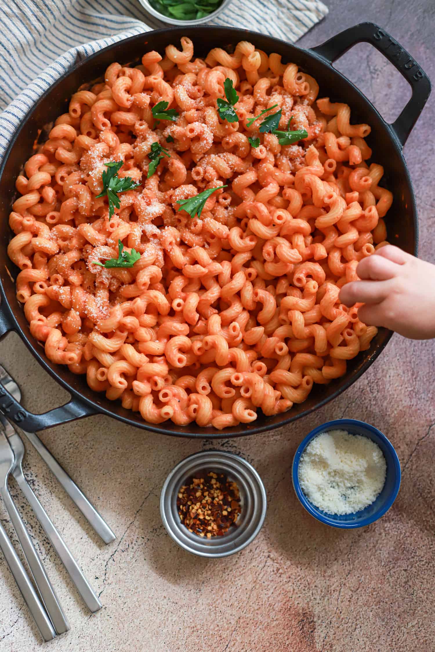 child's hand reaching for pasta in creamy tomato sauce.