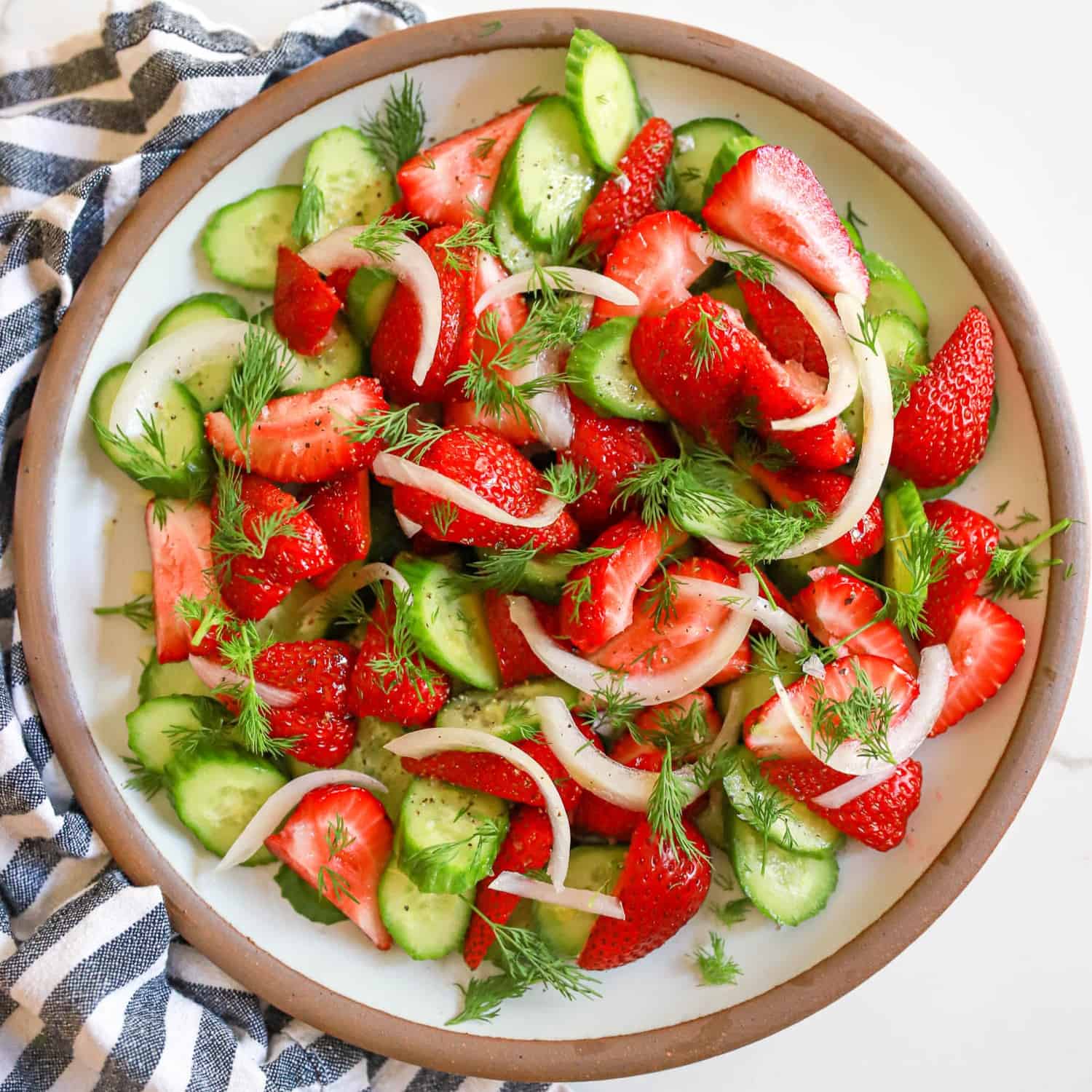 Round plate of strawberry cucumber salad with onions and fresh herbs.