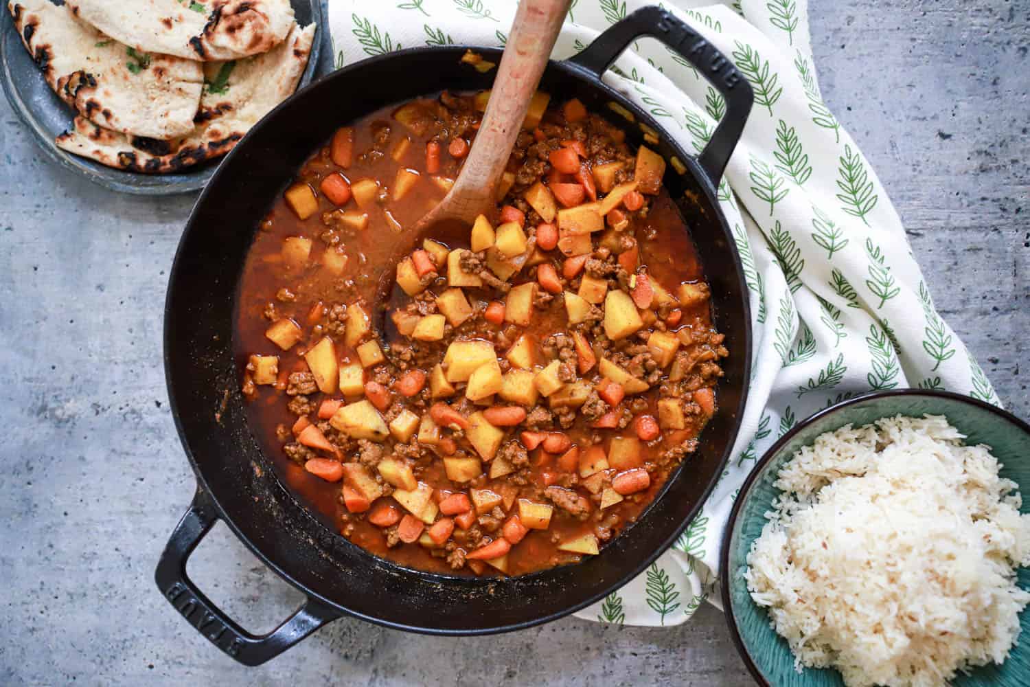 Large skillet of ground beef curry with rice and naan on the side.