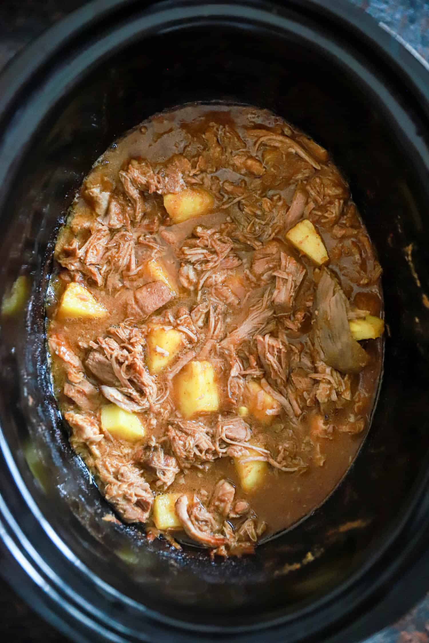 Slow cooker al pastor with pineapple chunks in a dark slow cooker bowl.
