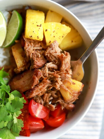 Close up top view of shredded slow cooker al pastor with pineapple and cilantro leaves.