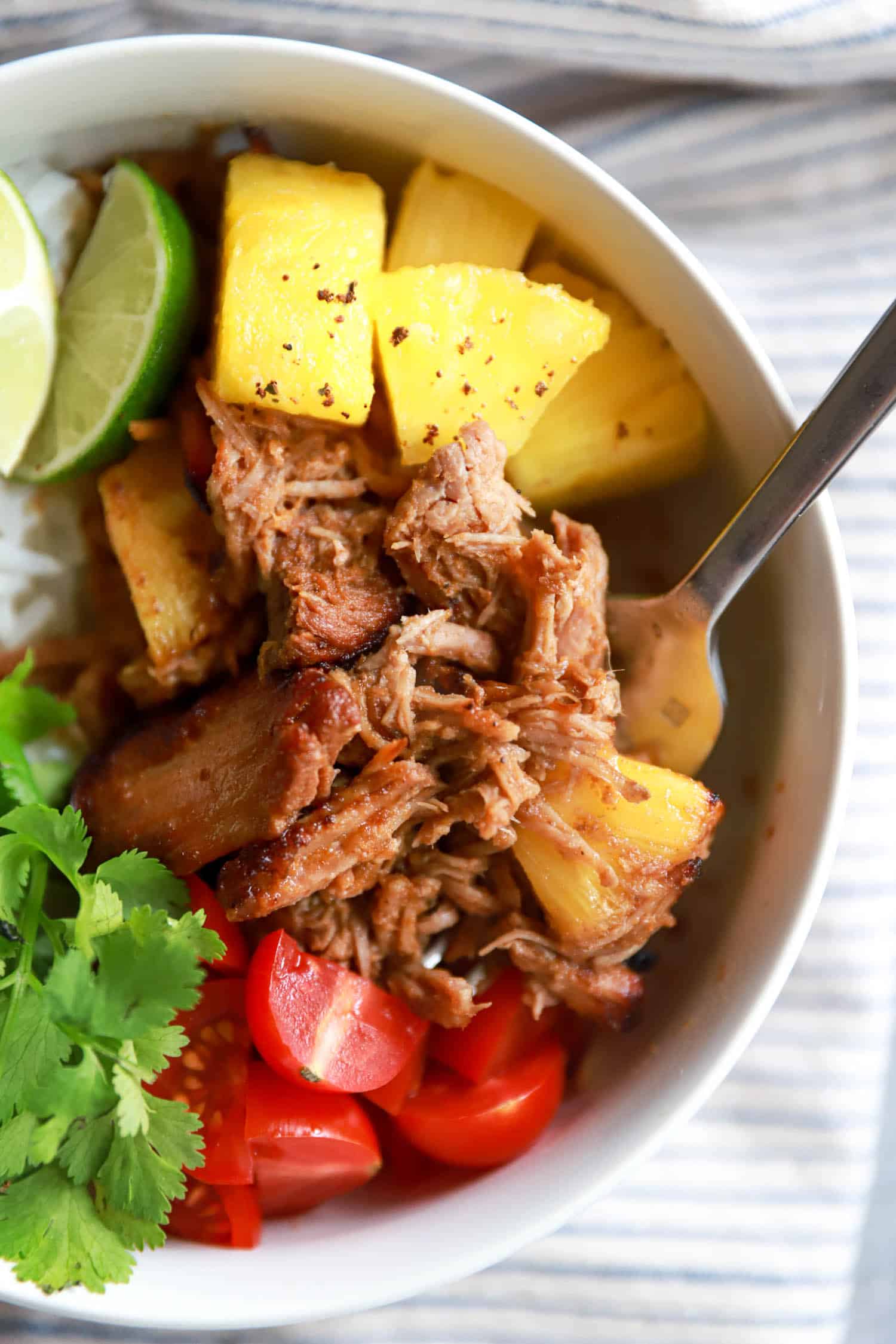Close up top view of shredded slow cooker al pastor with pineapple and cilantro leaves.