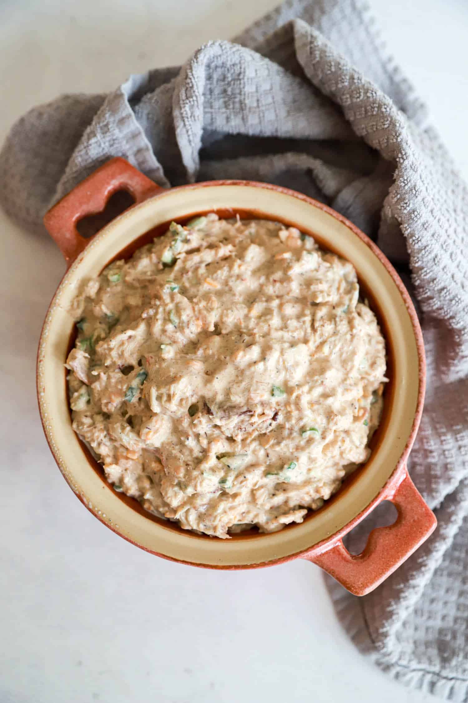 Unbaked crab dip in a small salmon colored round baking dish.