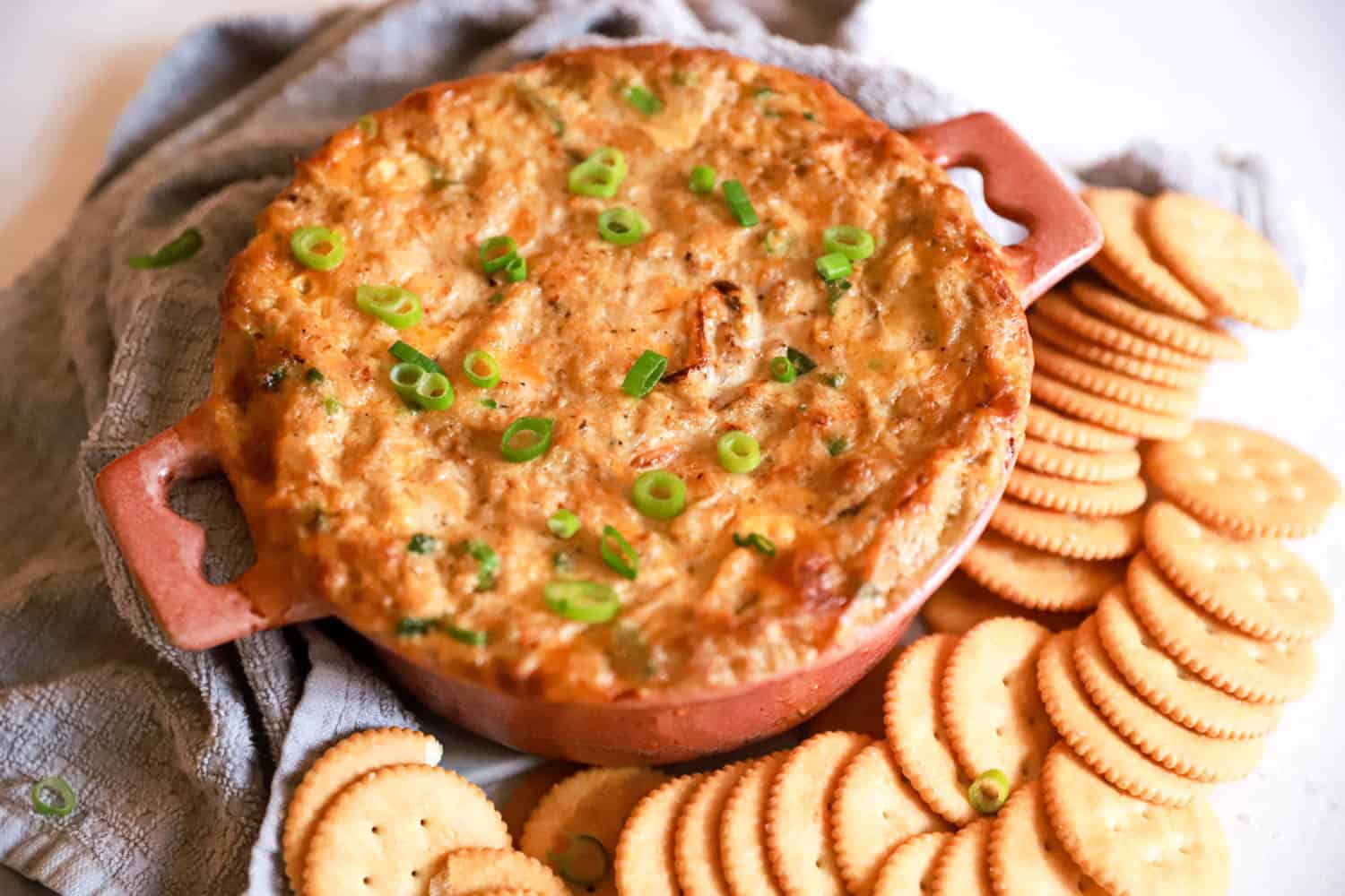 Round baking dish of hot crab dip surrounded by Ritz crackers.
