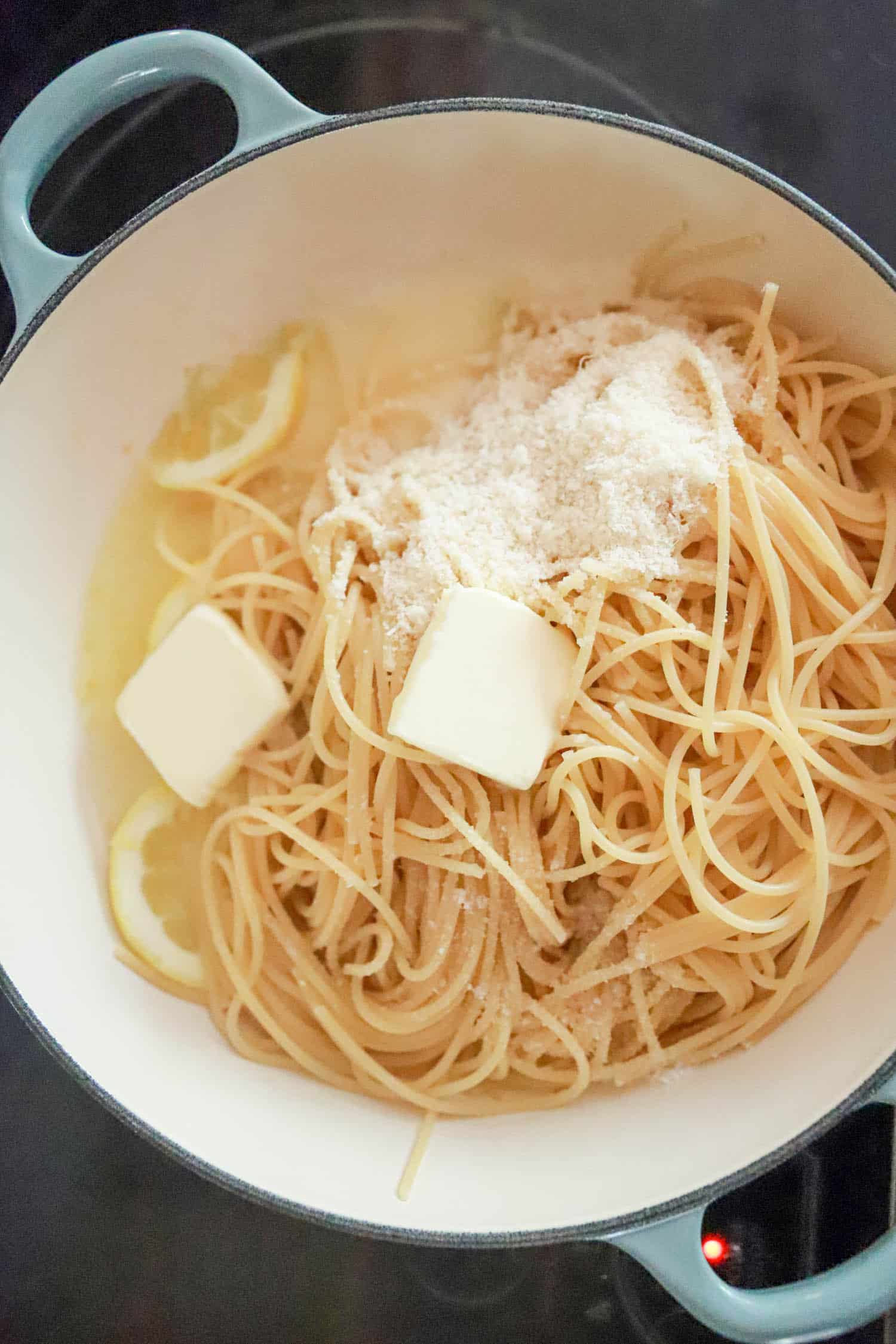 Cooked spaghetti with fresh parm and butter pats in a round white skillet.