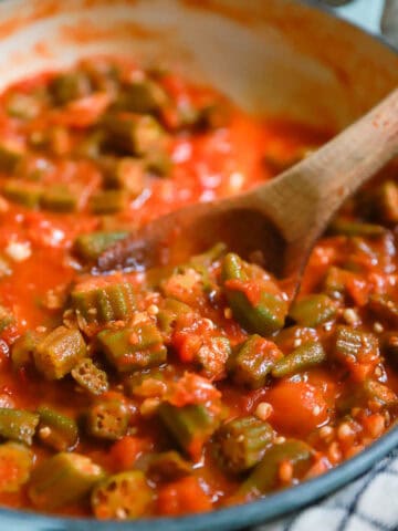Stewed okra and tomatoes in a skillet with a wooden spoon.