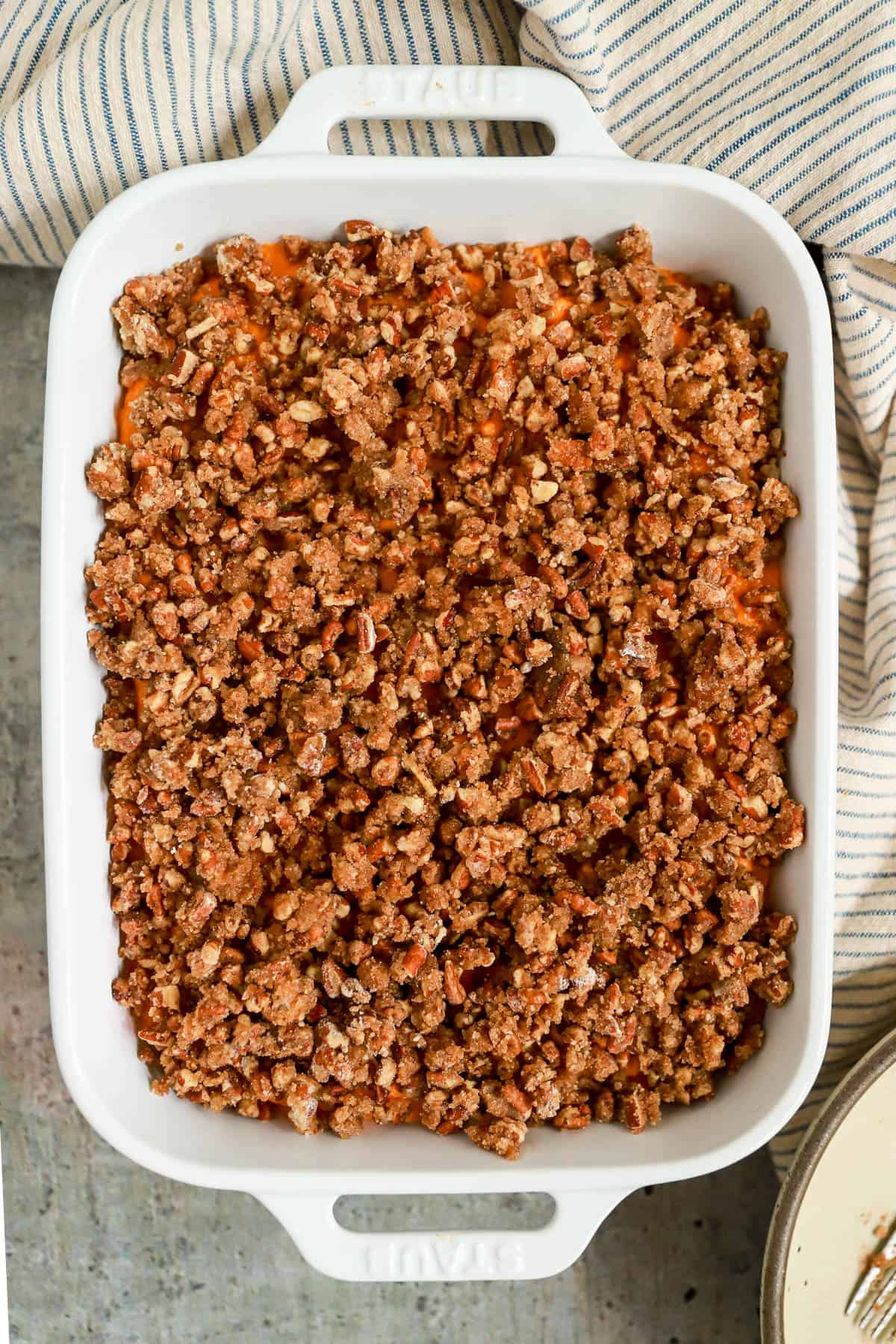 Unbaked carrot souffle recipe with brown sugar pecan topping in white baking dish.